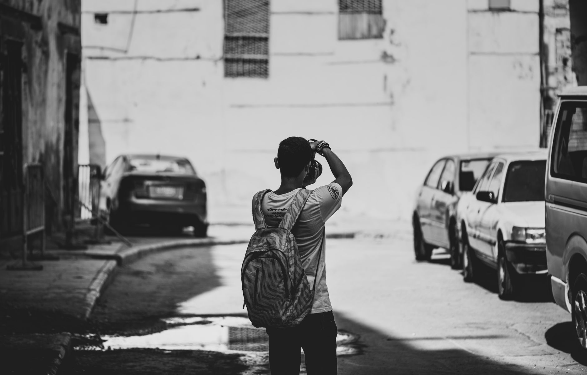 Un homme avec un sac à dos photographie la rue de la ville en noir et blanc.
