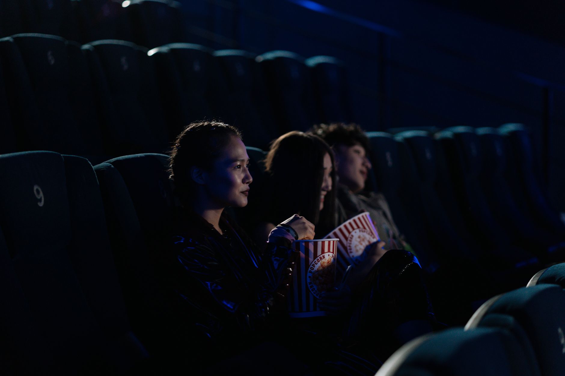 Groupe d'amis regardant un film dans un cinéma sombre, dégustant du pop-corn.