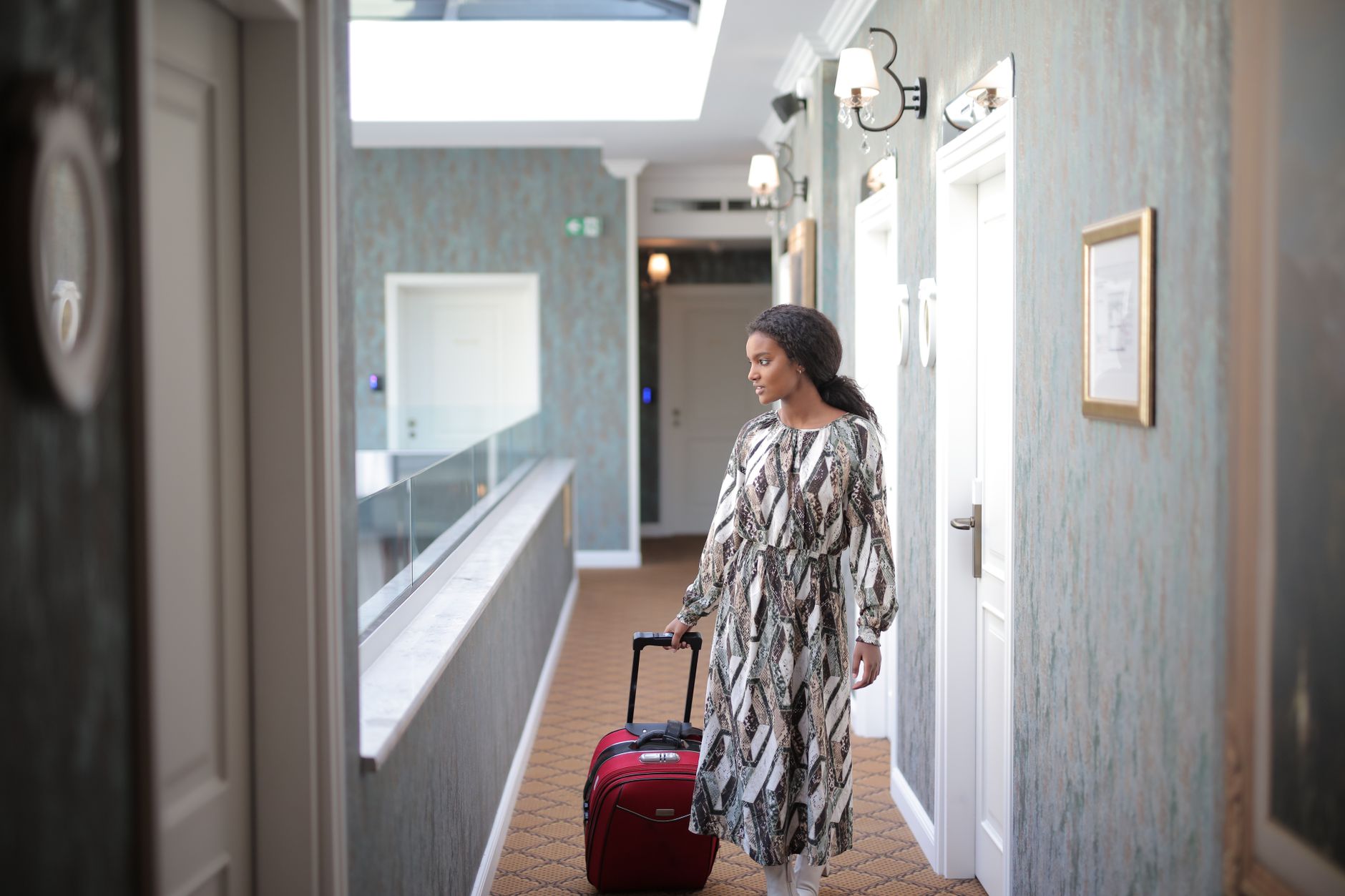 Une femme marche avec des bagages dans un couloir d'hôtel élégant, incarnant l'élégance du voyage.