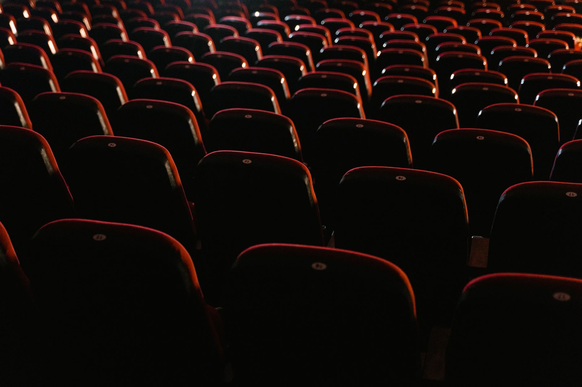 Rangs de sièges rouges vides dans une salle de cinéma faiblement éclairée, présentant un environnement de cinéma.