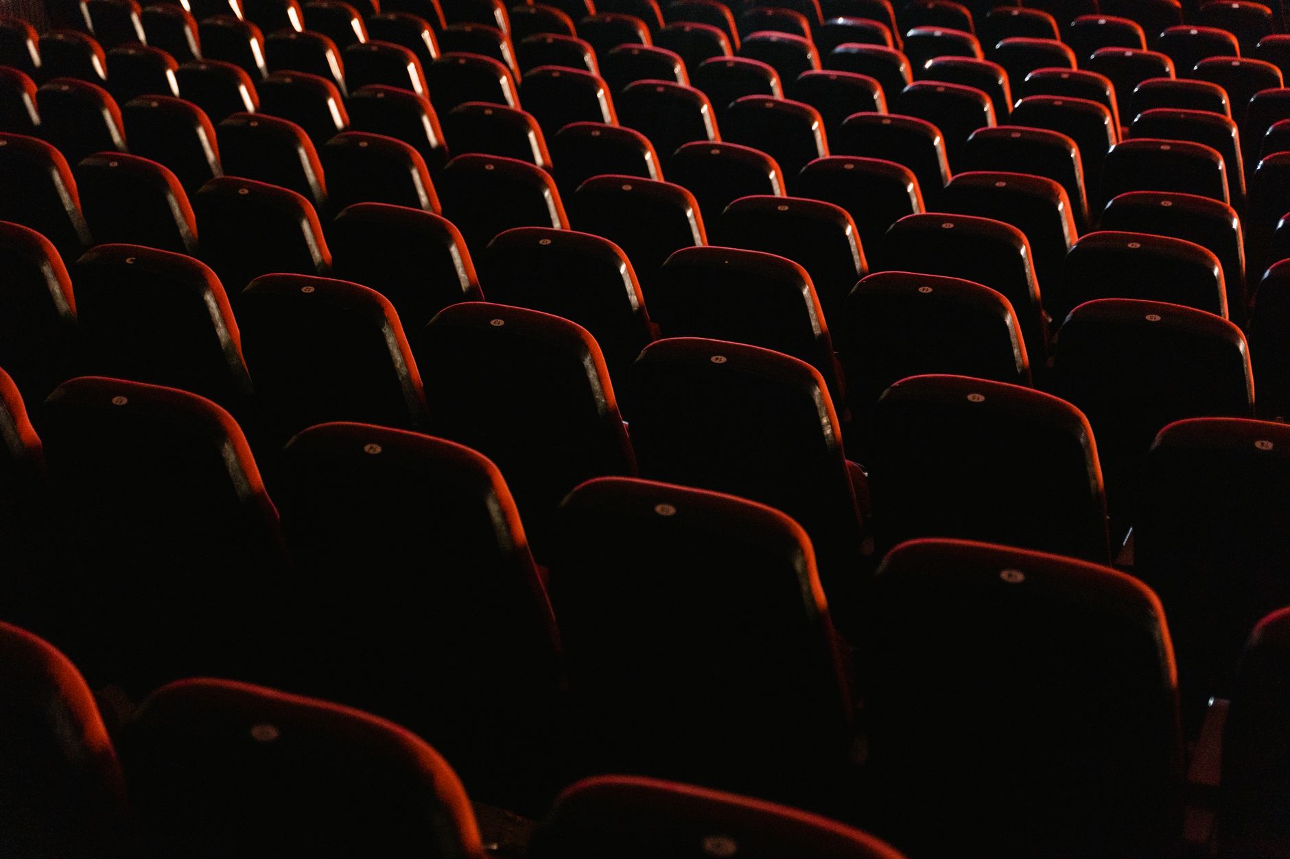 Une vue de sièges de théâtre rouges vides éclairés doucement, montrant l'ambiance calme d'un cinéma.