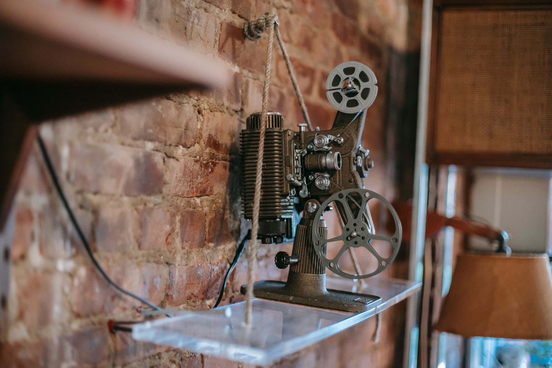 Ancien projecteur de cinéma mécanique exposé sur une étagère contre un mur en briques.