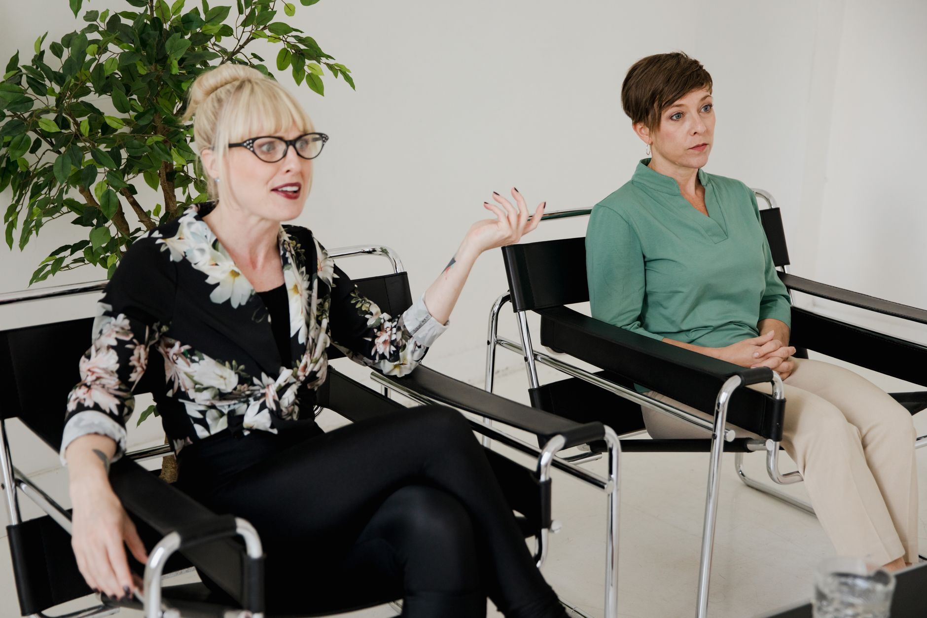 Deux femmes assises dans des fauteuils noirs, l’une parlant avec un geste de la main et l’autre écoutant.