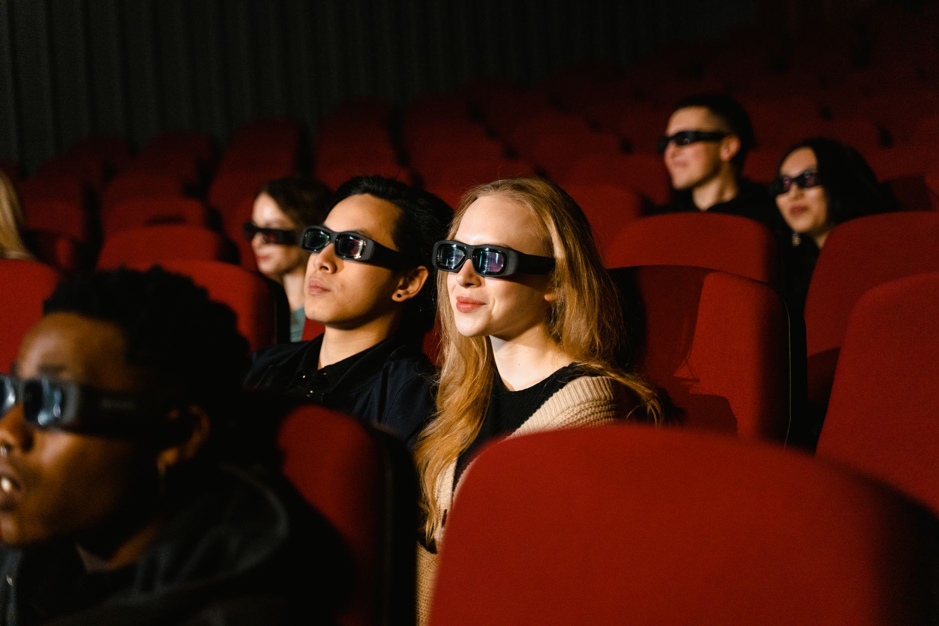 Plusieurs personnes assises dans les fauteuils rouges d’une salle de cinéma et portant des lunettes 3D.