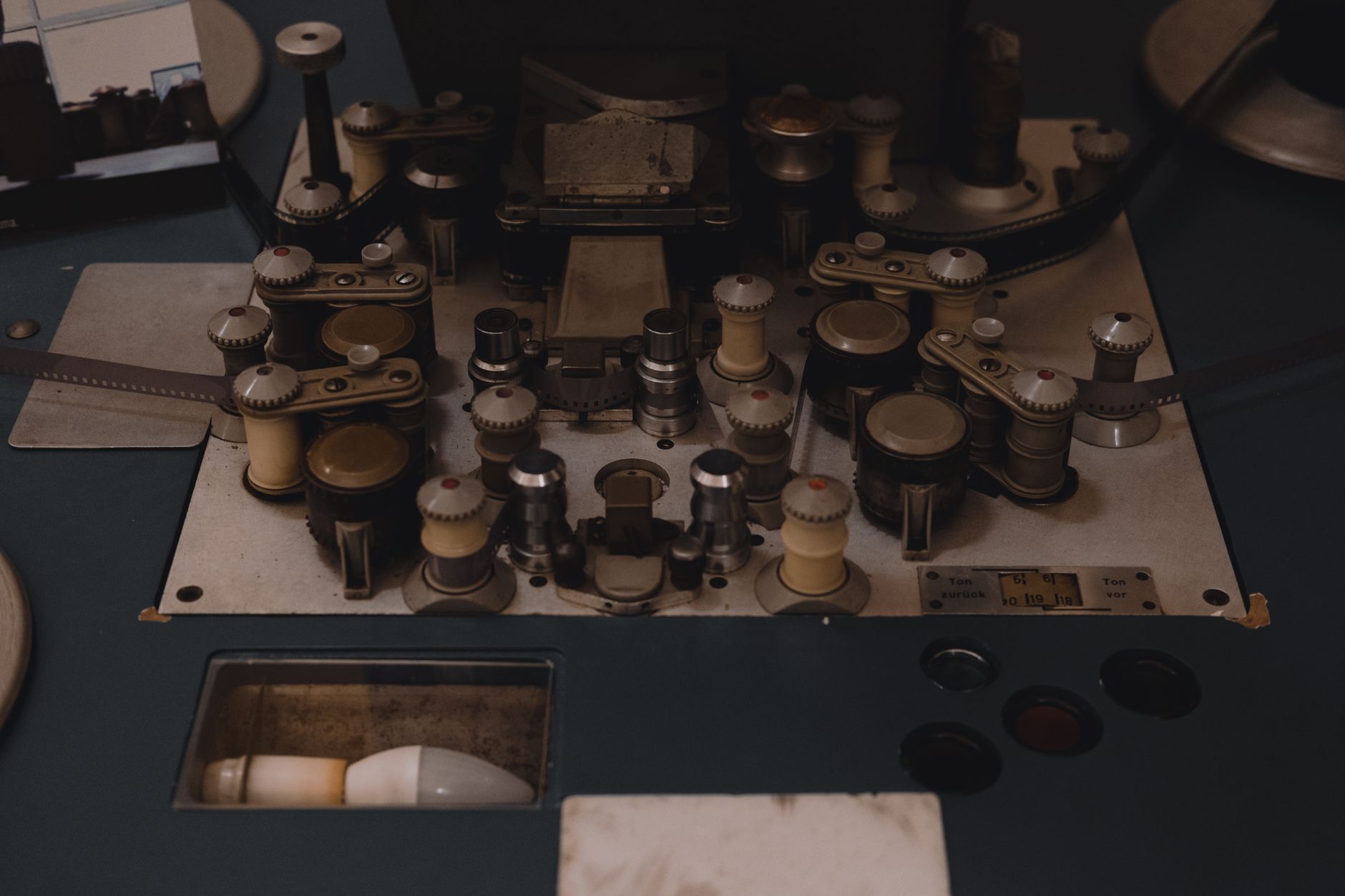 Vue en plongée d’un appareil ancien de cinéma avec pellicule passant sur des galets et rouleaux, ampoule dans un logement en bas à gauche.